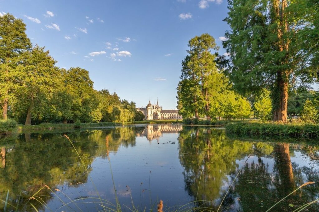 Journée des Plantes. Photo du château de Chantilly reflétant sur un lac entouré de forêt