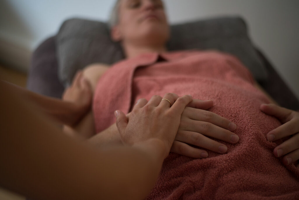 Photo de Jeanne Gaillard en train de tenir la main d'une femme allongée sur une table de massage.